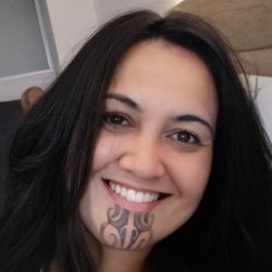 Headshot of Māori woman with long dark hair, moko kauae (sacred Māori chin tattoo) and smiling.