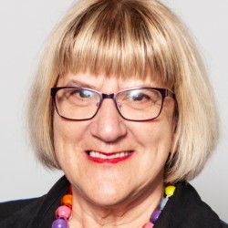 Headshot of a blonde woman with bob hairstyle, with glasses and red lipstick, smiling.